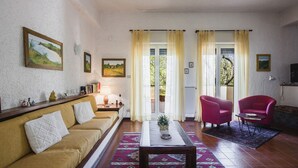 A living room with a sofa, a coffee table, and two chairs. There are curtains on the windows, and a door leading outside. - Pedara Escape With Garden by Wonderful Italy (Pedara)
