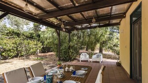 An outdoor patio with a wooden table set for dining, surrounded by chairs, and a covered area with hanging lights. - Pedara Escape With Garden by Wonderful Italy (Pedara)