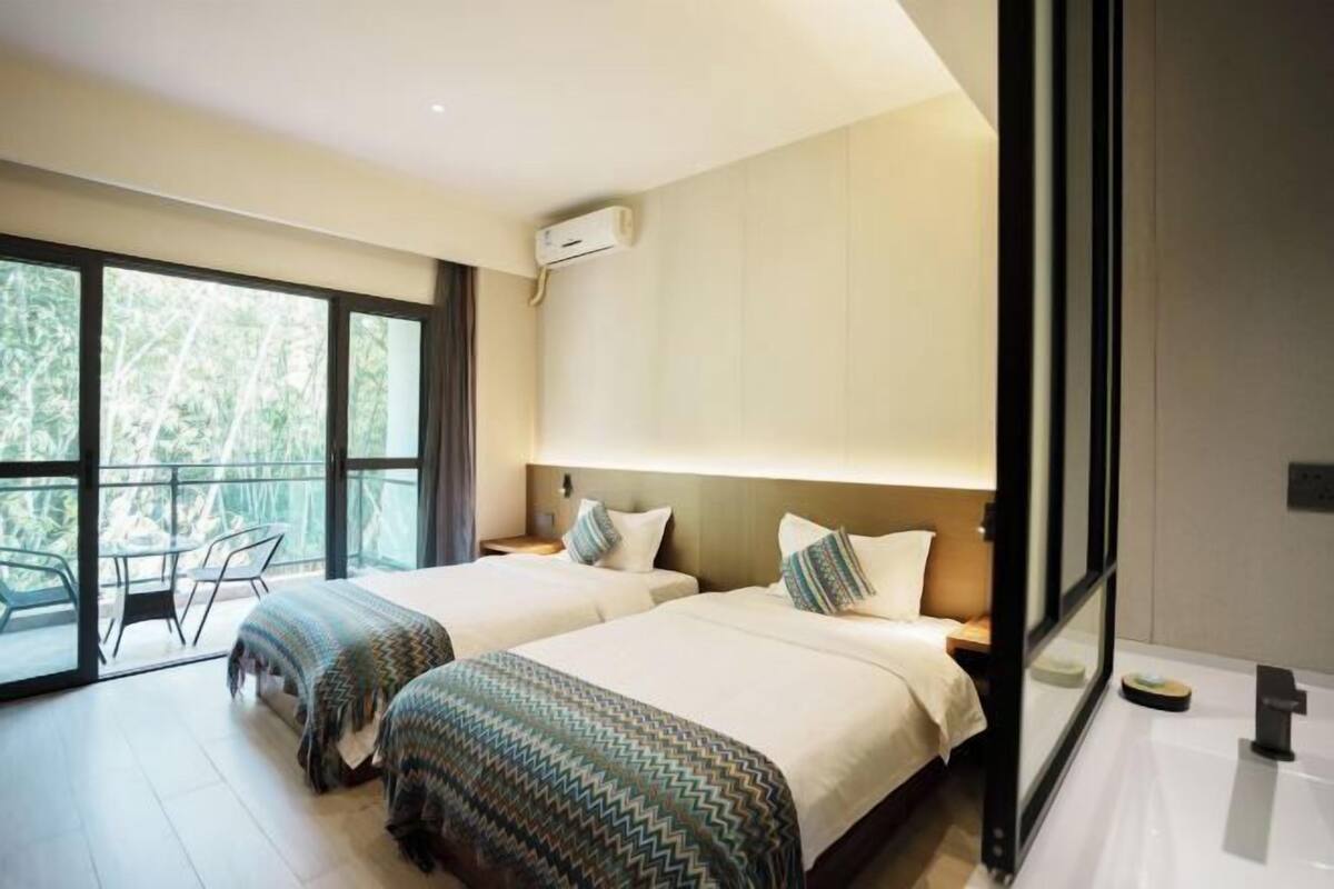 A modern hotel room with two beds, a balcony with a table, and an air conditioning unit.