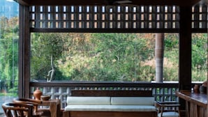 A wooden deck with a bench and chairs, overlooking a forested area. - Nanlahe Paya Resort Hotel (Mengla)