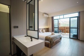 A modern bedroom with a large bed, a bathroom with a white sink, and a sliding glass door leading to an outdoor area. - Nanlahe Paya Resort Hotel (Mengla)