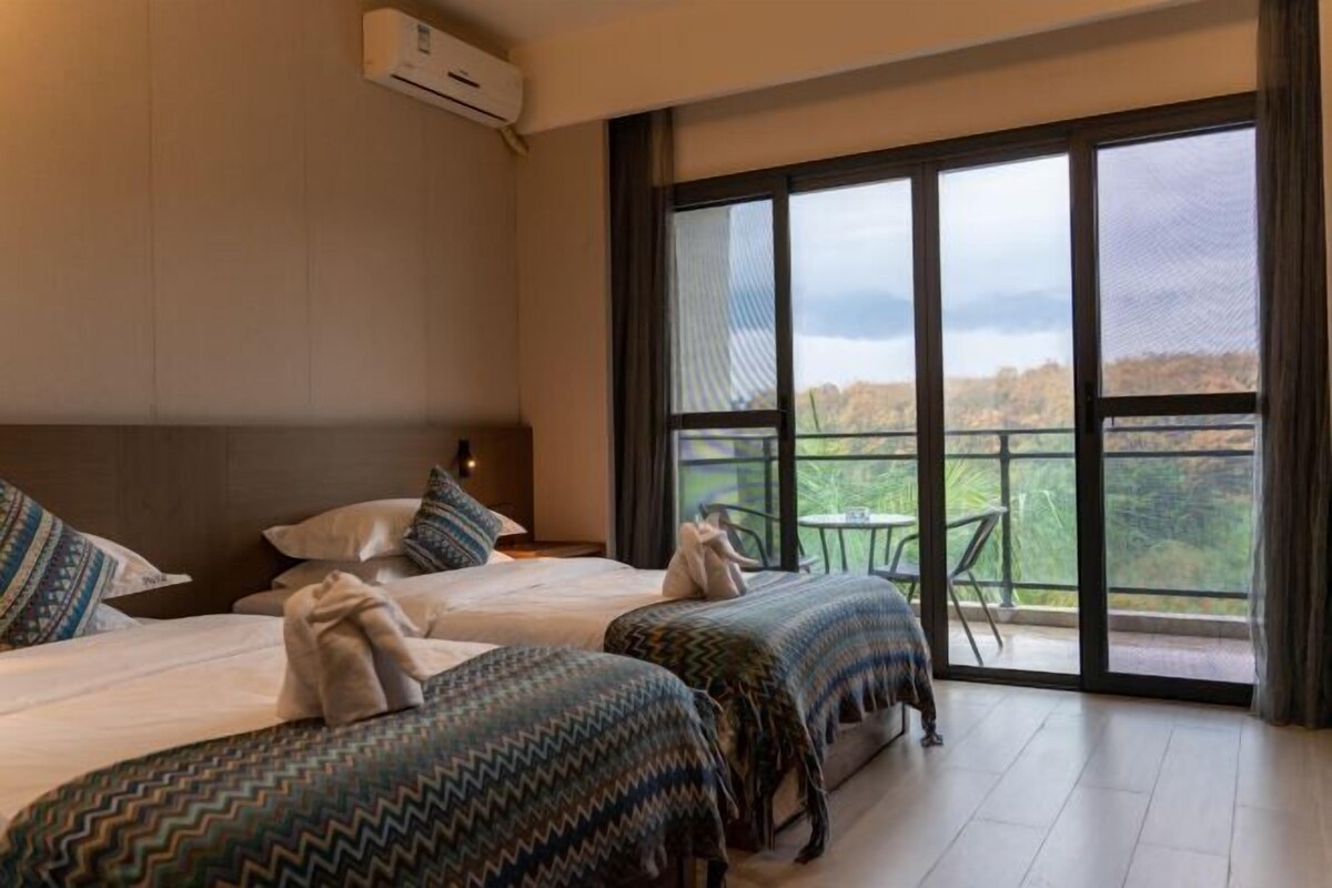 A hotel room with two beds, a balcony with a table and chairs, and a large window.