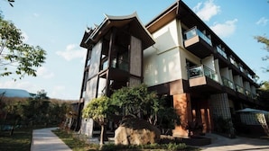 A modern building with a traditional architectural style, featuring balconies and a pathway leading to the entrance. - Nanlahe Paya Resort Hotel (Mengla)