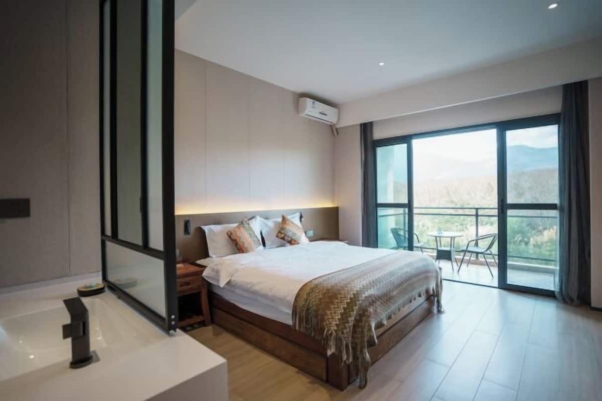 A modern bedroom with a large bed, a bedside table, a built-in bench, and a balcony with a view.