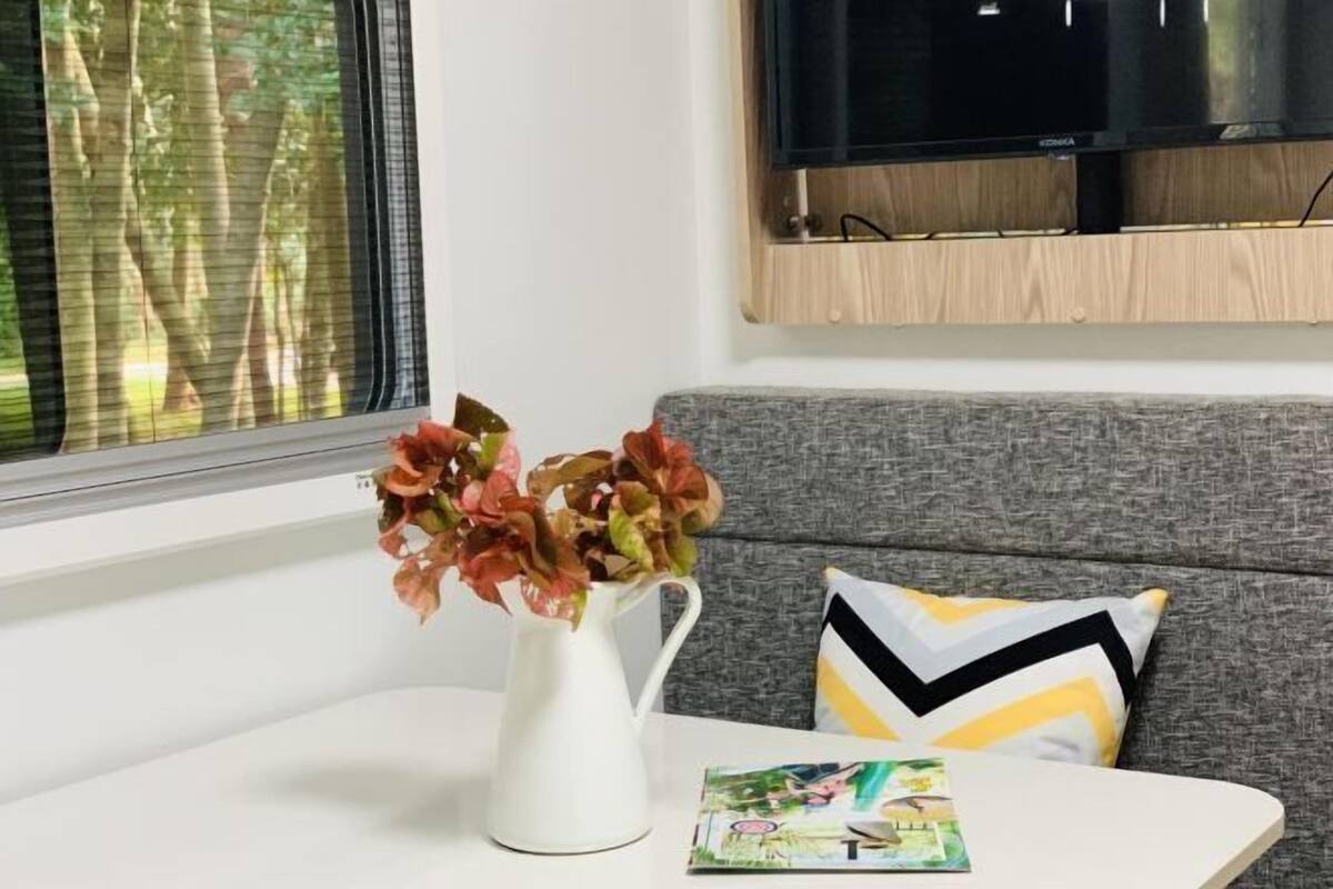 A room with a grey sofa, a white table, a white vase with flowers, and a television mounted on the wall.
