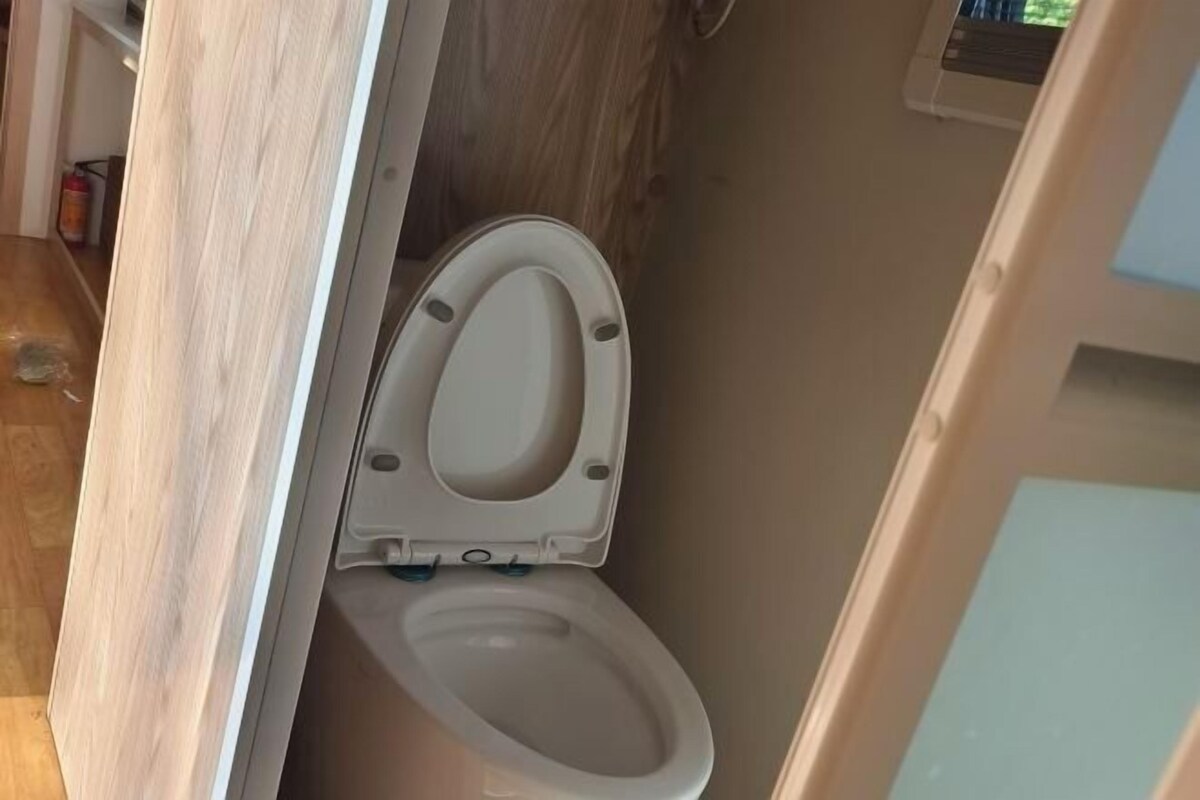 A bathroom with a toilet, wooden flooring, and a visible fire extinguisher.