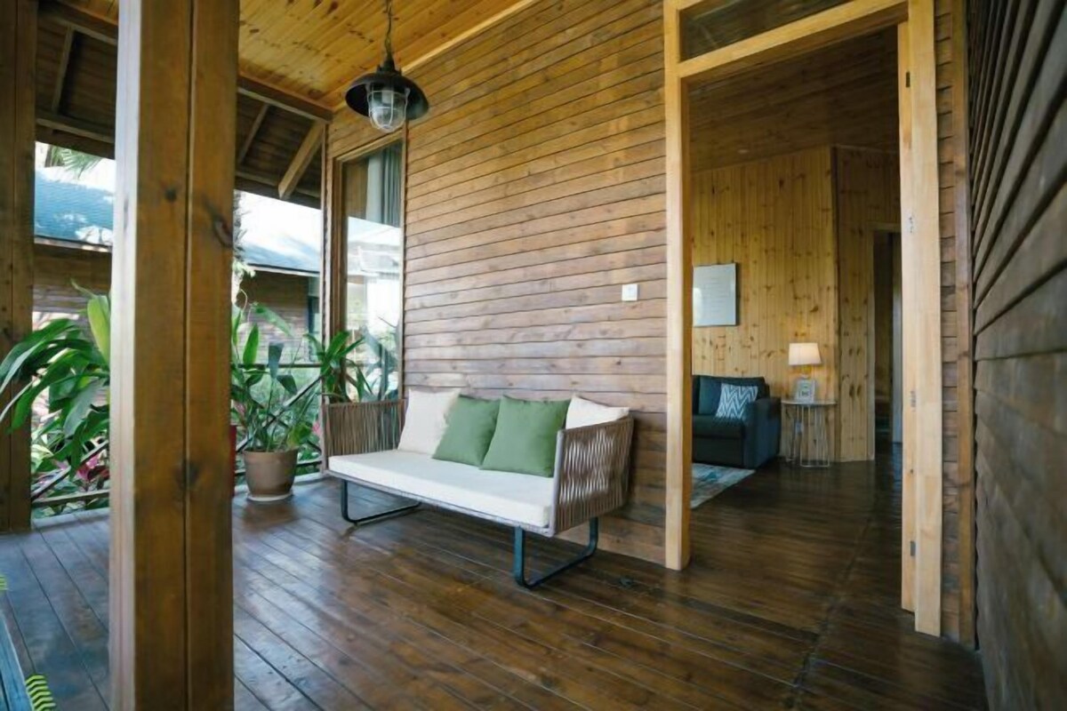 A wooden interior with a sofa, a hanging light fixture, and a view of the outdoors.