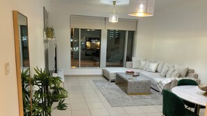 A modern living room with a sofa, coffee table, and chairs. There is a large window with a view of the city.