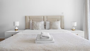A neatly made bed with a folded towel, two bedside tables with lamps, and a headboard with decorative pillows.