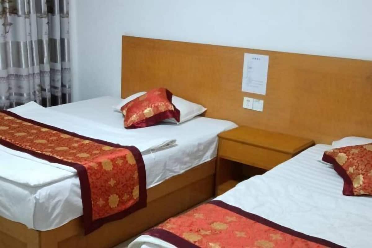 Ett hotellrum med två separata sängar, var och en med ett rött och guldmönstrat överkast, vita kuddar och en sänggavel i trä.