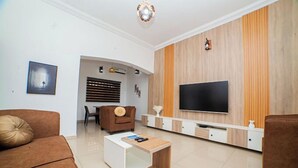 A modern living room with a flat-screen TV, brown sofas, a coffee table, and a wooden accent wall. - Schemes Apartment Portharcourt (Port Harcourt)