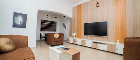 A modern living room with a flat-screen TV, brown sofas, a coffee table, and a wooden accent wall.