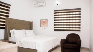 A bedroom with a bed, a chair, and a wall-mounted air conditioner. - Schemes Apartment Portharcourt (Port Harcourt)