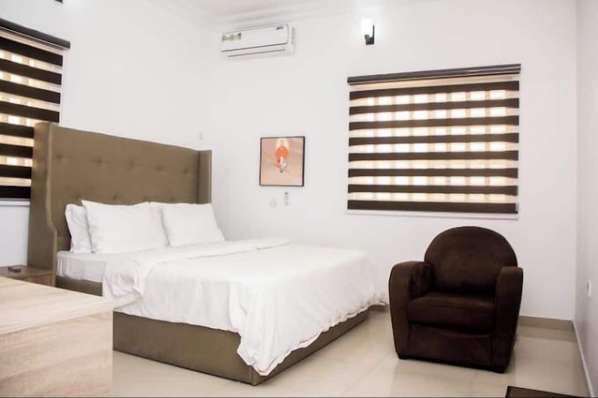 A bedroom with a bed, a chair, and a wall-mounted air conditioner.
