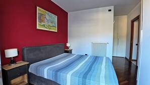 A bedroom with a bed, two bedside tables, a nightstand, a radiator, and a door leading to another room. - Como Apartment + Free parking & WiFi (Como)