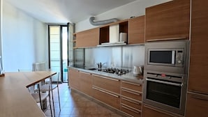 A modern kitchen with stainless steel appliances, wooden cabinets, and a dining area with a table and chairs. - Como Apartment + Free parking & WiFi (Como)