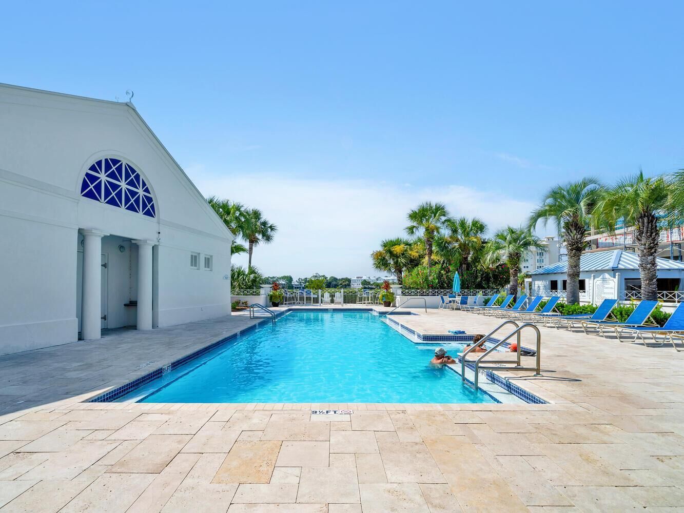 A swimming pool with a clear blue water, surrounded by lounge chairs and palm trees.