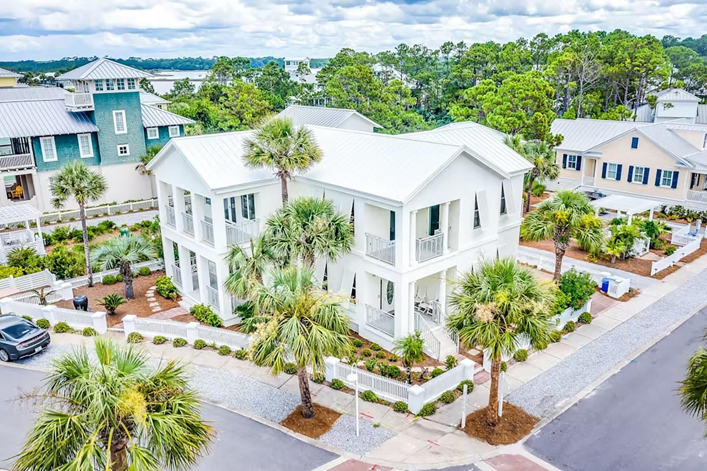 A two-story white building with a balcony, surrounded by palm trees and a white fence.