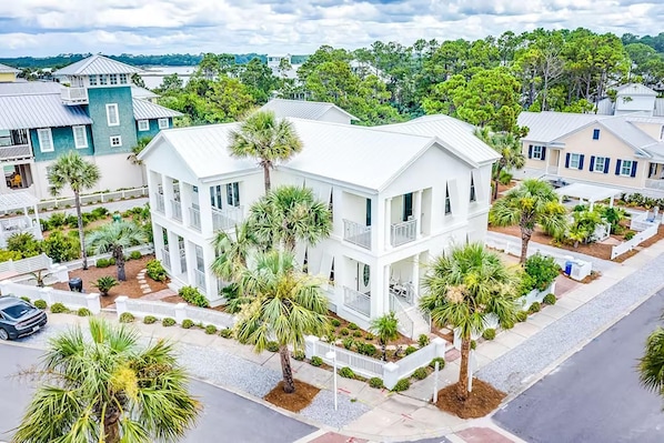 A two-story white building with a balcony, surrounded by palm trees and a white fence.