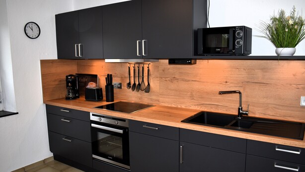 Une cuisine moderne avec des meubles de couleur noire, un plan de travail en bois, un four à micro-ondes encastré et une machine à café.
