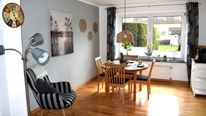 Un coin repas avec une table et des chaises en bois, un fauteuil à rayures, une lampe sur pied et une vue sur l’extérieur par une fenêtre.
