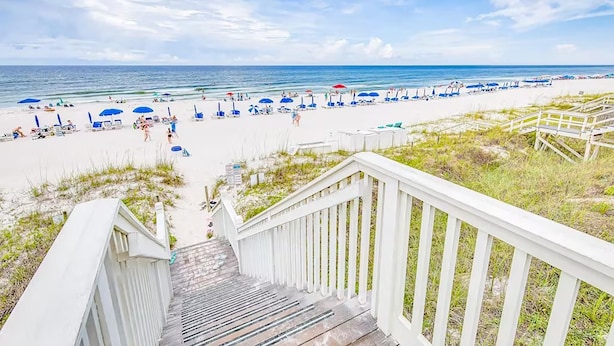A beach with a wooden staircase leading down to the sand, surrounded by beach umbrellas and lounge chairs. - Relax Awhile (Panama City Beach)