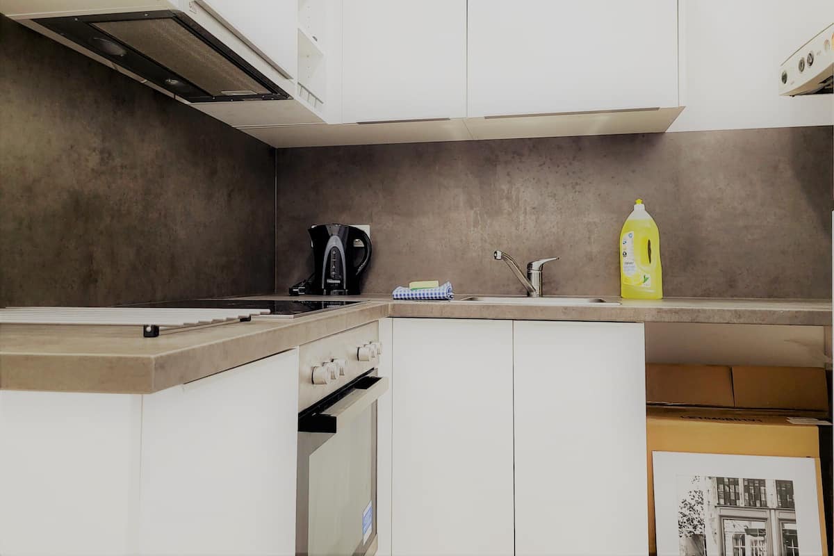 Een keuken met witte kastjes, een zwarte koffiezetapparaat, een roestvrijstalen kraan en een gele afwasmiddel.