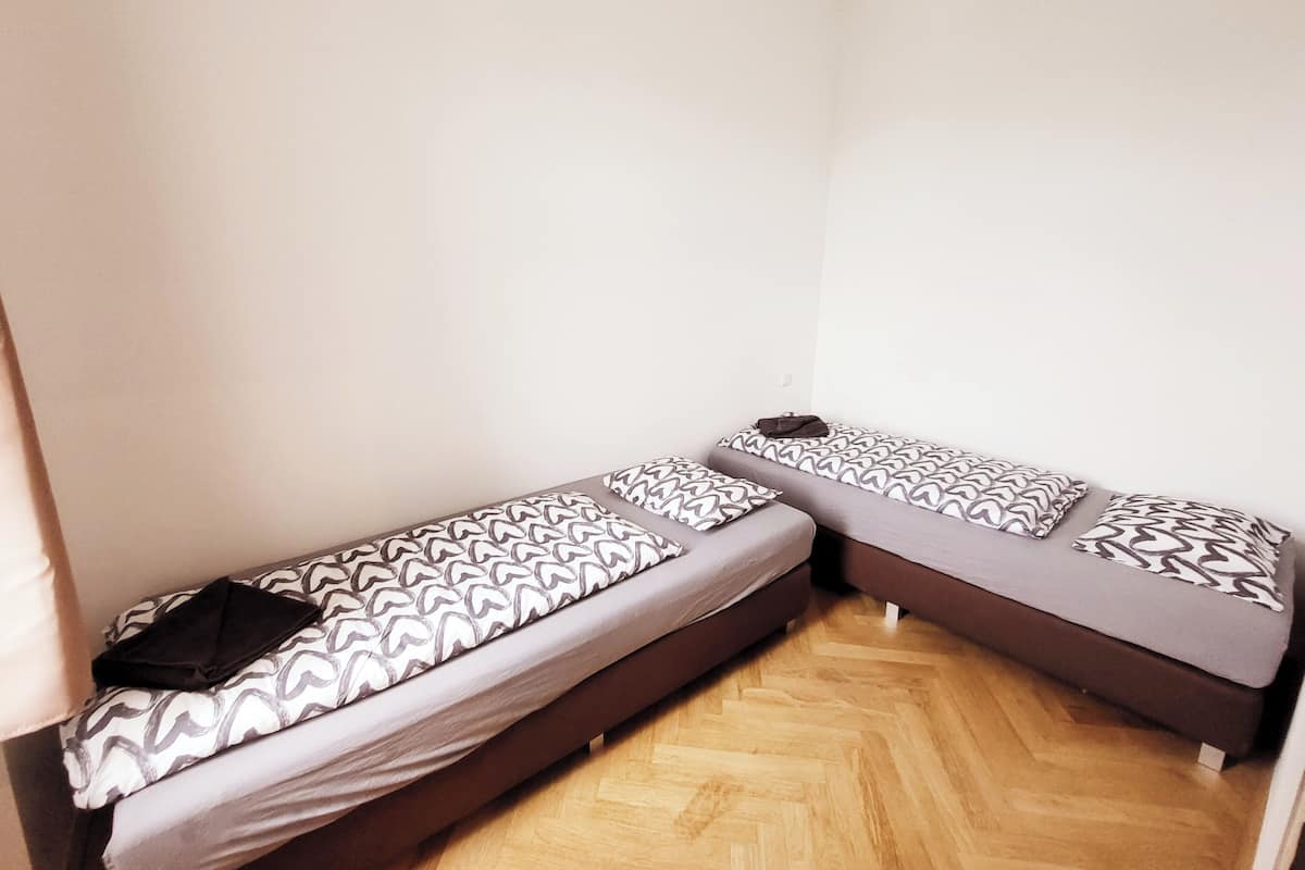 A room with two single beds, each with patterned bedding and a pillow.
