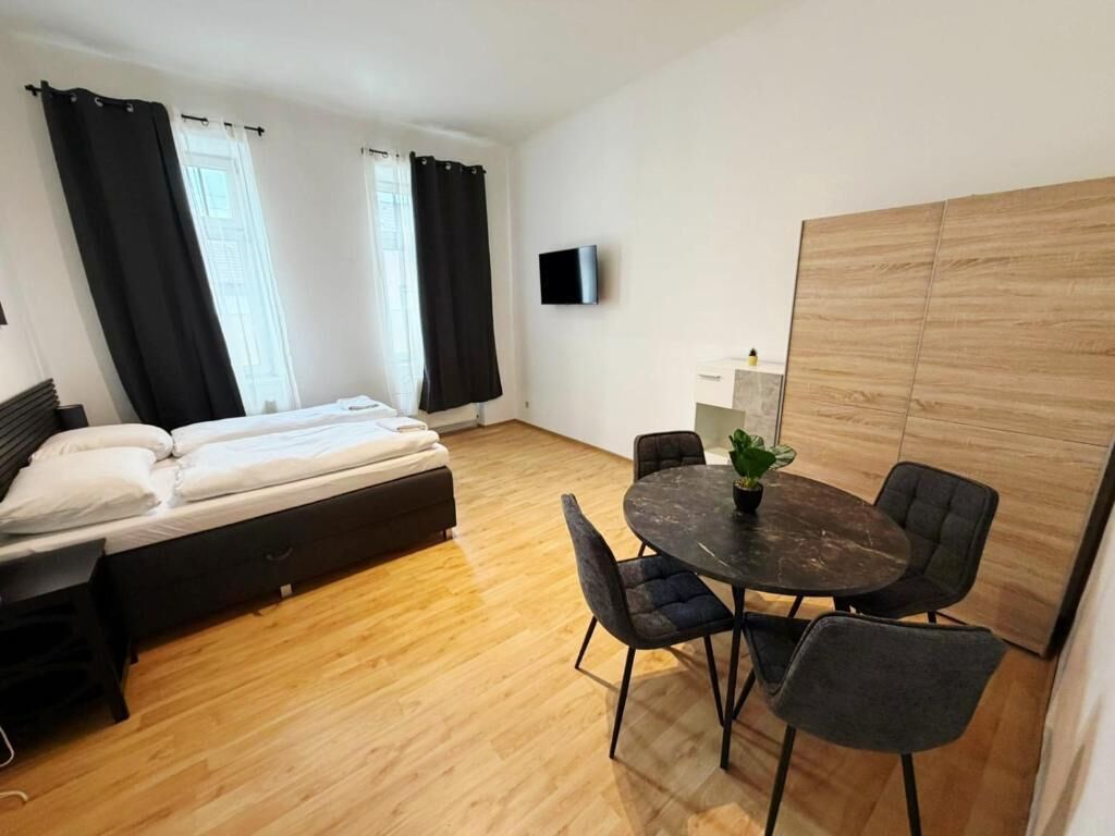 Een kamer met een bed, een ronde tafel met stoelen, een televisie aan de muur en een houten scheidingswand.