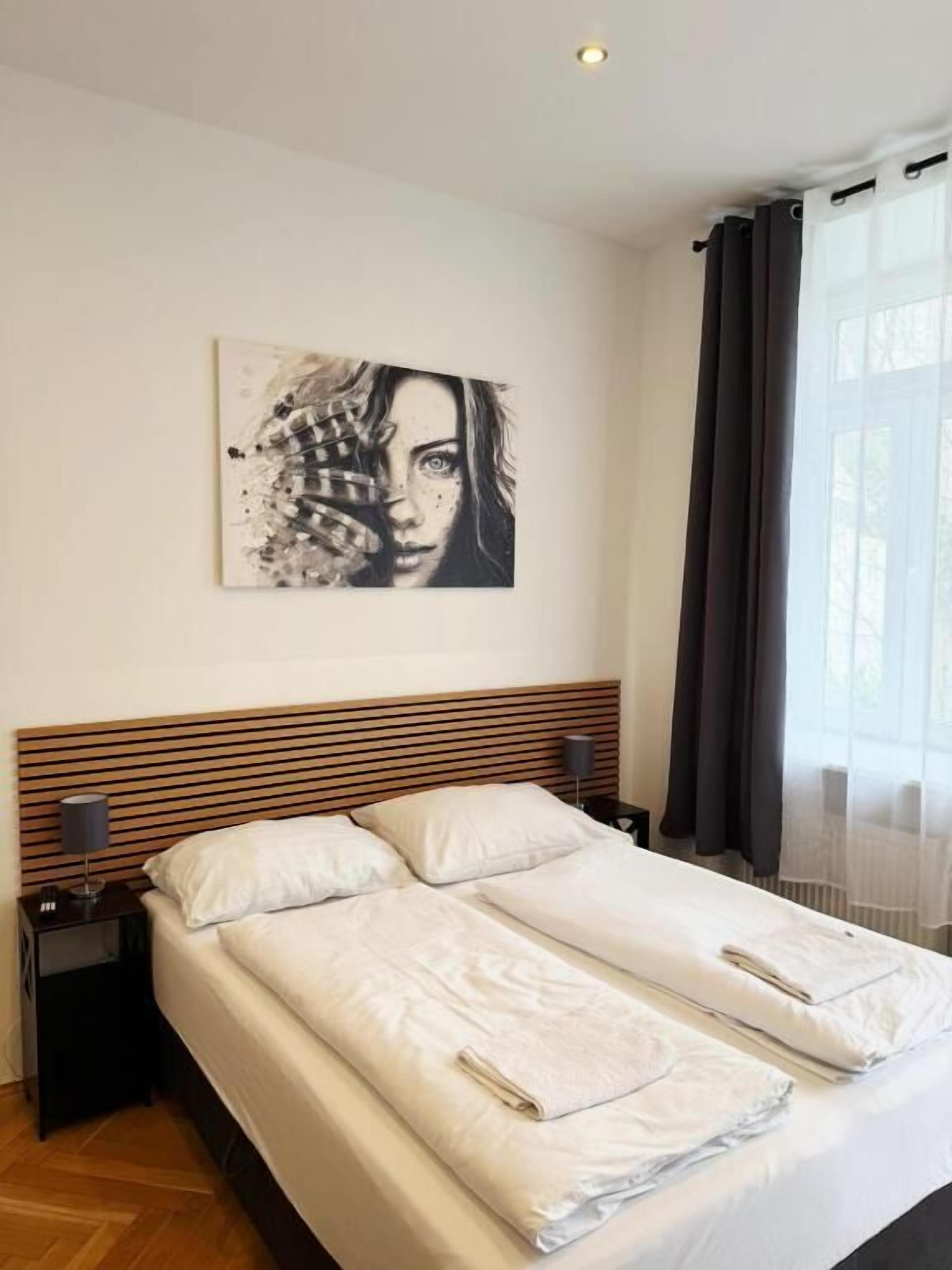 A double bed with a wooden headboard, a bedside table with a lamp, and a wall-mounted artwork.