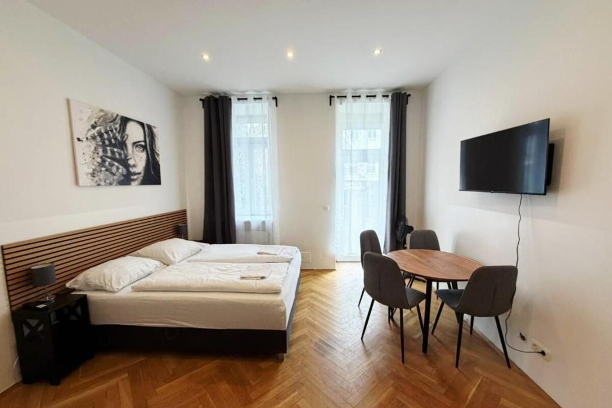 Habitación de hotel con cama, televisión, mesa de comedor con sillas y un cuadro en la pared.