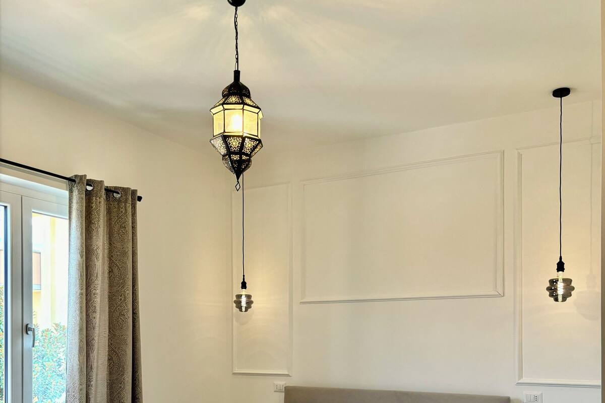 A bedroom with a bed, two bedside lamps, a window with curtains, and a radiator.