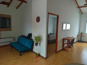 A room with a sofa, a small table, a potted plant, a mirror, and a bed in the background. - Manila Apartaestudios  (Medellín)
