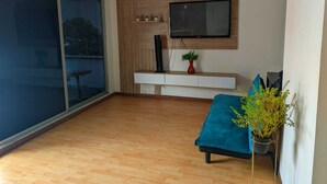 A modern living room with a sliding glass door, a mounted TV, a wooden bench, and a potted plant. - Manila Apartaestudios  (Medellín)