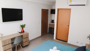 A bedroom with a bed, a desk with a chair, a TV, and a wardrobe. - Manila Apartaestudios  (Medellín)