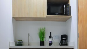 A compact kitchen with wooden cabinets, a microwave, a coffee maker, and a sink. - Manila Apartaestudios  (Medellín)