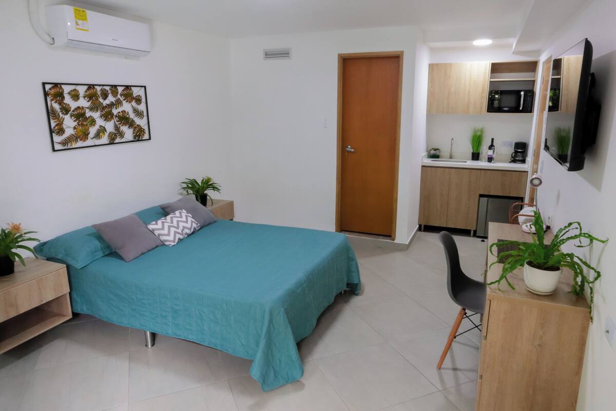 A bedroom with a bed, bedside tables, a desk, a chair, a microwave, a sink, and a door.