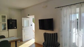 Ein Zimmer mit Holzboden, einem gestreiften Sessel, einem an der Wand montierten Flachbildfernseher, einem Tisch mit Stühlen, einem Schrank mit Glastüren und einer Tür, die nach draußen führt.