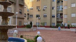 A courtyard with a fountain, surrounded by multi-story buildings with balconies and air conditioning units.
