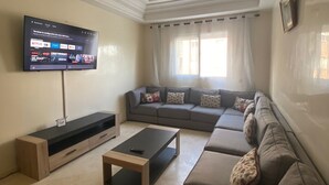 A living room with a flat-screen TV, a sofa, a coffee table, and a window with curtains.