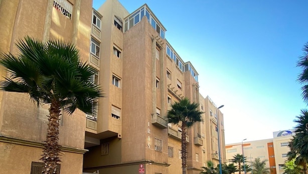 A building with a beige facade, multiple balconies, and palm trees.