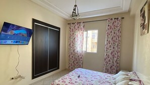 A bedroom with a bed, a TV mounted on the wall, a wardrobe, and a window with curtains.