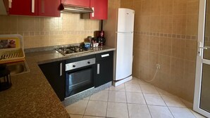 A kitchen with red cabinets, a white refrigerator, a gas stove, and a sink.