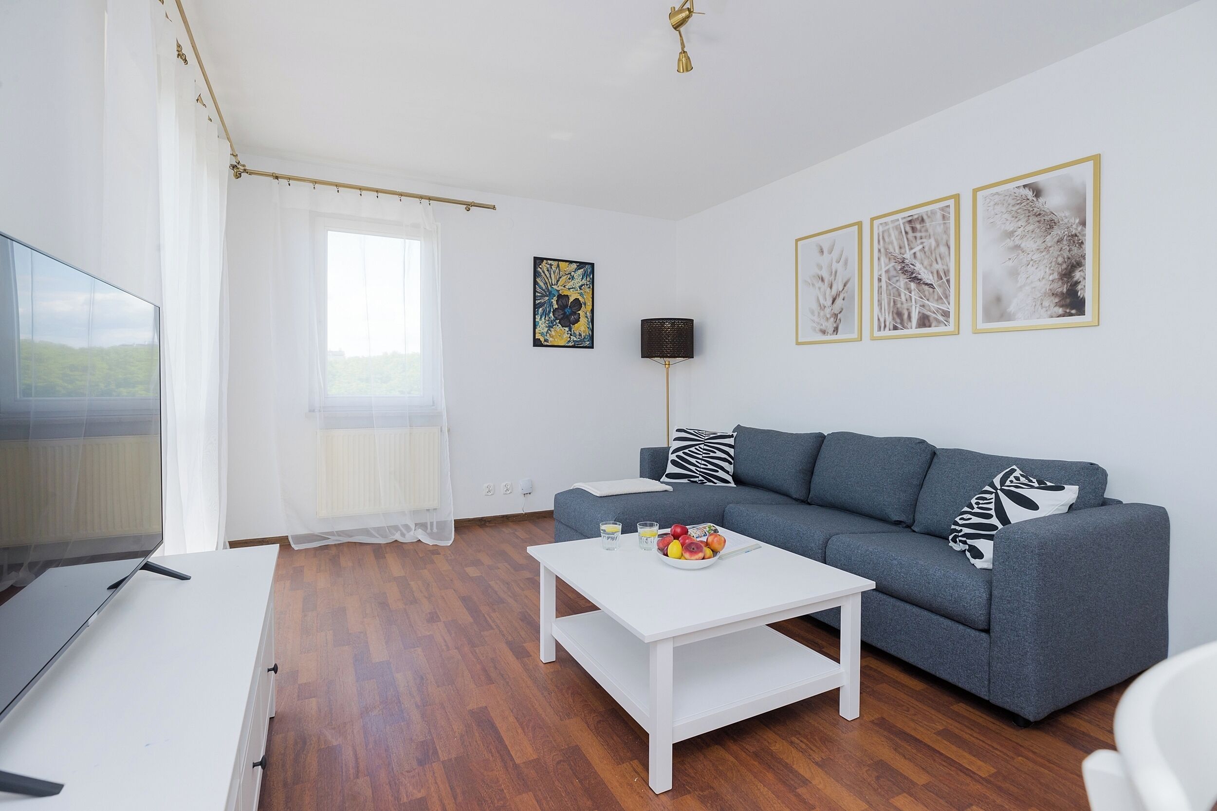 A modern living room with a grey sofa, white coffee table, and a flat-screen TV.