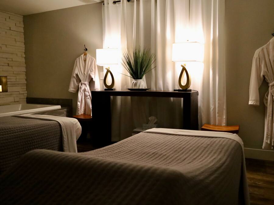 A hotel room with two beds, a small table with a plant, and two robes hanging on hooks.