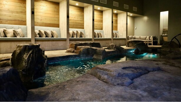 A spa area with a pool, wooden benches, and a seating area with cushions. - Xhale Resort and Spa (Idaho Falls)