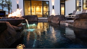 A swimming pool with a waterfall feature, surrounded by rocks and a fire pit. - Xhale Resort and Spa (Idaho Falls)