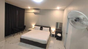 A modern hotel room with a large bed, bedside tables, a standing fan, and a seating area with a chair. - Hillview Terrace (Hat Yai)