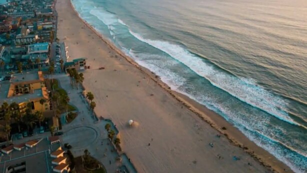 Vista aérea de una zona costera con playa, edificios y cielo despejado.
