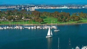 Un puerto deportivo con barcos, un puente al fondo y un paisaje urbano al otro lado del agua.